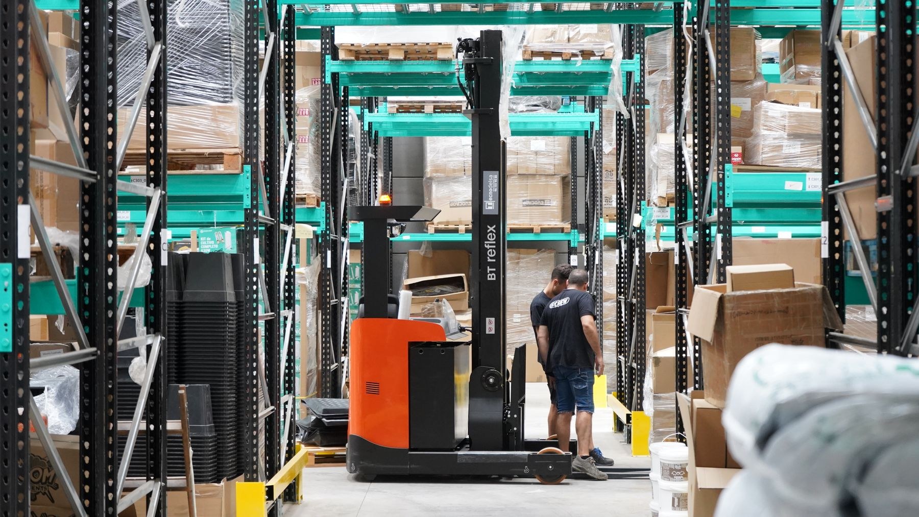 Warehouse staff beside a forklift and stacked goods in storage aisles